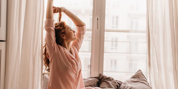 Cute female model in pink pajama enjoying morning. Pleasant ginger woman sitting on bed.